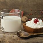 Ein Glas Milch und eine Portion Milchreis mit Krische in einer Holzschale mit Holzlöffel
